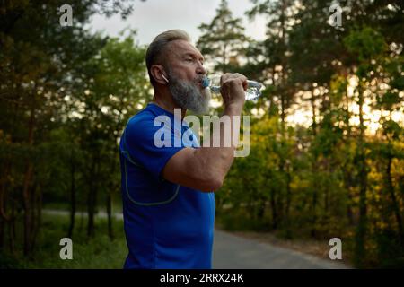 Ein älterer, pensionierter Läufer, der während des Trainings eine Pause mit Trinkwasser einlegt Stockfoto