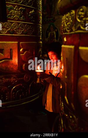 Ein frommer buddhistischer Pilger betet zwischen Gebetsmühlen und hält eine Dkar Me (Butterlampe) im Boudhanath-Tempel in Kathmandu, Nepal. Stockfoto