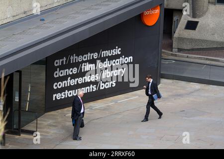 Zwei Geschäftsleute in formellen Anzügen vor dem Haupteingang des Barbican Centre in der City of London am Freitag, den 24. August 2012. Vor dem Hintergrund der ikonischen Brutalistik-Architektur des EC2-Anwesens hält die Szene ein professionelles Treffen während des geschäftigen Sommers der Olympischen Spiele 2012 in London fest. Zu dieser Zeit war das Barbican ein wichtiger kultureller Drehpunkt für das „London 2012 Festival“ und veranstaltete Weltklasse-Ausstellungen und -Aufführungen für ein internationales Publikum Stockfoto