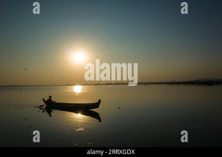 Die Silhouette des Fischerbootes gegenüber der Sonne am Taung Tha man Lake bei Sonnenuntergang. Amarapura, Mandalay, Myanmar Stockfoto