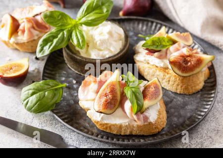 Toast oder Bruschetta mit Speck und Feigen, Frischkäse und Honig auf grauem Steinhintergrund. Italienisches Vorspeisenrezept. Stockfoto