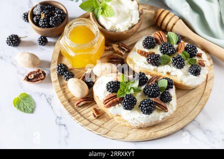 Keto Diet Sandwiches, Imbiss. Süße Bruschetta mit Käse und Beeren, brombeerricotta und Honig auf Marmortisch. Gesunde Frühstückstoasts. Stockfoto