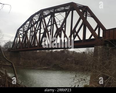 Eine rustikale Eisenbahnbrücke aus Metall, die sich über die Breite eines ruhigen Flusses erstreckt und zwei Seiten der Landschaft verbindet Stockfoto