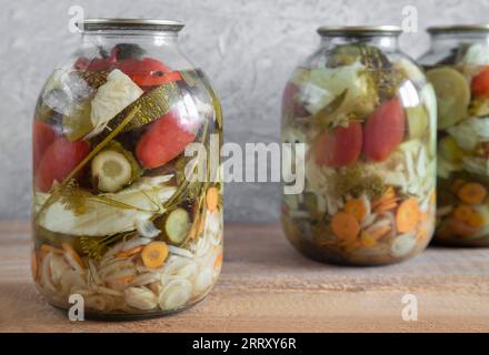 Verschiedene Gemüsesorten werden in Glasgefäßen konserviert: Gurken, Tomaten, Kohl, Zwiebeln, Karotten, Zucchini. Vorderansicht, Nahaufnahme. Stockfoto