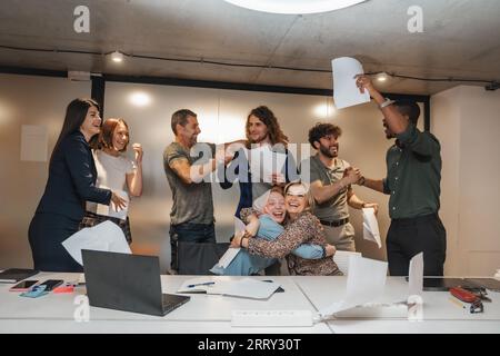 Geschäftsleute mit unterschiedlichen Altersgruppen, die sich gegenseitig umarmen und gemeinsamen Geschäftserfolg feiern. Geschäftsleute feiern erfolgreich spät in der Nacht Stockfoto