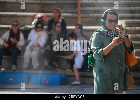 Teheran, Iran. September 2023. Eine Frau nutzt ihr Handy, während ihr Kind am Sommerfest des Kinderwasserspiels im GMAX Adrenaline Park im Nordwesten Teherans teilnimmt. Der g-Max Adrenaline Park ist der erste Adrenalinpark im Iran. Dieser Unterhaltungskomplex umfasst eine kostenlose Sprungmatte (großer Sprung), einen Abenteuerpark (aufgehängte Leiter), eine Schaukel und Bungee-Jumping. (Bild: © Rouzbeh Fouladi/ZUMA Press Wire) NUR REDAKTIONELLE VERWENDUNG! Nicht für kommerzielle ZWECKE! Stockfoto