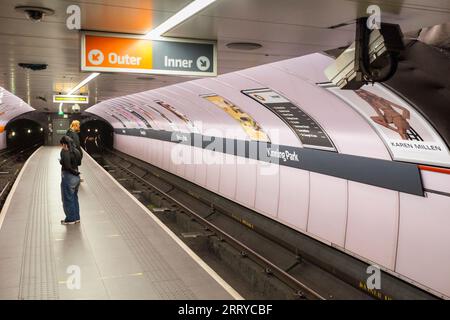 Kinning Park Station an der SPT Glasgow U-Bahn zeigt den schmalen Inselbahnsteig und wartende Passagiere mit den Lichtern eines nahenden Zuges Stockfoto