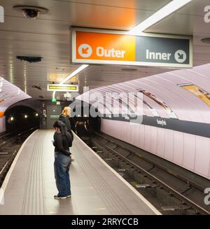 Kinning Park Station an der SPT Glasgow U-Bahn zeigt den schmalen Inselbahnsteig und wartende Passagiere mit den Lichtern eines nahenden Zuges Stockfoto