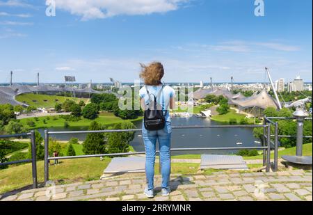 Junge Frau Touristen schaut auf Olympiapark im Sommer, München, Deutschland. Dieser Ort ist ein berühmtes Wahrzeichen der Stadt Munchen. Reisekonzept, Tourismus Stockfoto