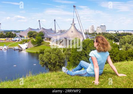 Junge Frau ruht im Sommer im Olympiapark in München. Dieser Ort ist ein berühmtes Wahrzeichen der Stadt Munchen. Konzept von Reisepersonen, Tourismus, Sport Stockfoto