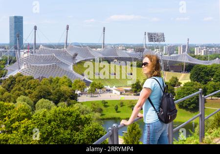 Junge Frau touristisch besucht Olympiapark im Sommer, München, Deutschland. Dieser Ort ist ein berühmtes Wahrzeichen der Stadt Munchen. Reisekonzept, Tourismus und Seufzen Stockfoto