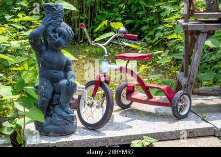 Ein altes rotes Dreirad steht draußen auf einer Gartenstatue im Hof Stockfoto