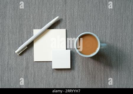 Bürobedarf. Notizblock, Stift, Tasse Kaffee auf grauem Stoffhintergrund. Draufsicht, Kopierbereich. Arbeitsbereich Stockfoto