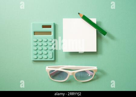 Grüner Taschenrechner und weißer Notizblock, farbiger Bleistift, Brille auf grünem Hintergrund. Draufsicht Stockfoto