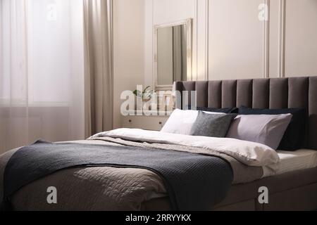 Komfortables Bett mit Kissen und Bettwäsche in stilvollem Zimmer. Innendesign Stockfoto