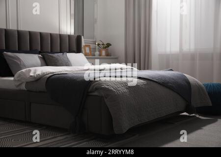 Komfortables Bett mit Kissen und Bettwäsche in stilvollem Zimmer. Innendesign Stockfoto