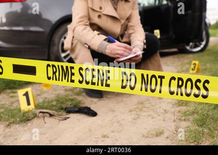 Professioneller Detektiv, der den Tatort im Freien untersucht, konzentriert sich auf gelbes Band Stockfoto