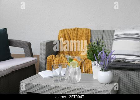 Tisch mit Buch, Wasserkanne, Topfpflanzen und Sofas auf der Außenterrasse Stockfoto