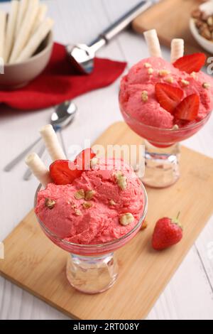 Köstliche Schaufeln Erdbeereis mit Waffelstäbchen und Nüssen in Glas-Dessertschüsseln, serviert auf weißem Holztisch, Blick über den Himmel Stockfoto