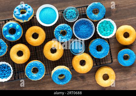 Mehrere schlichte und blaue Bonbons in Schokolade getauchte Donuts mit Schüsseln mit Streuseln. Stockfoto