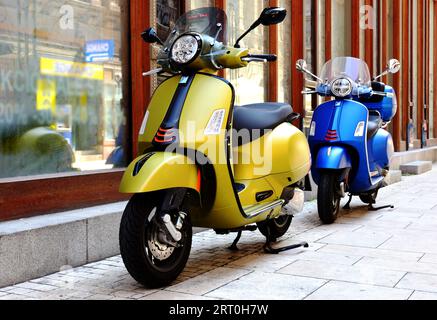 Roter, italienischer Roller oder Moped im Vintage-Stil, der entlang der alten Stuckhausaußenwand auf dem Bürgersteig geparkt ist. Städtische Szene. Glasfenster. Holzrahmen Stockfoto
