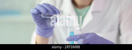 Eine weibliche Wissenschaftlerin mit Handschuhen hält zwei Reagenzgläser mit Flüssigkeit in der Nähe. Stockfoto