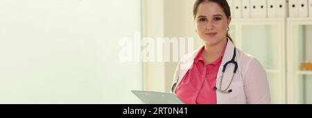 Junge, freundliche Ärztin, die ein Klemmbrett mit medizinischen Dokumenten, Stift und in die Kamera schaut. Stockfoto