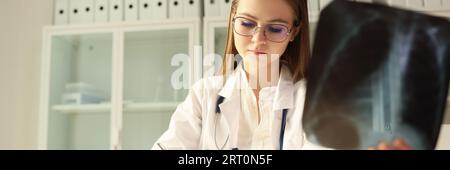Junger Brillenarzt prüft Röntgenaufnahmen und macht Notizen in medizinischen Dokumenten. Stockfoto