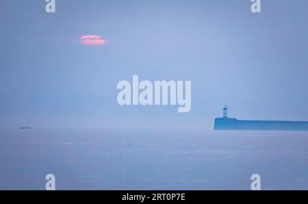 Sonnenuntergang hinter dem Dunst des Newhaven-Leuchtturms und der niedrigen Wolke vom Seaford Beach an der Ostküste von Sussex im Südosten Englands Stockfoto