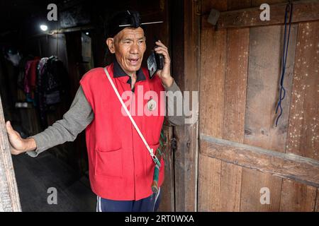 Ein älterer Mann des Apatani-Stammes, der traditionelle gewebte Kleidung und eine markante Schirmmütze trägt, in einem ländlichen Dorf im Ziro-Tal, Indien. Stockfoto