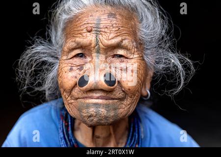 Frau aus dem Apatani-Stamm in einem Haus aus einem kleinen Dorf in der Nähe von Ziro, mit traditionellen Gesichtstattoos und traditionellen Nasenstöpseln, Ziro, Indien Stockfoto