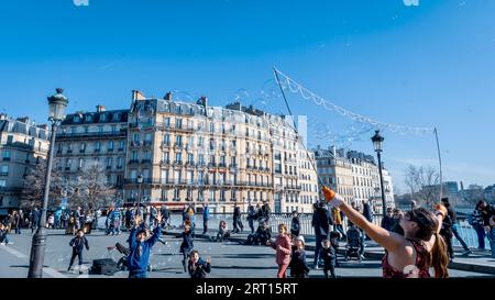 Eine lächelnde junge Frau steht in einem städtischen Park und blickt zum Himmel, während sie einen hellen, bunten Drachen in den Händen hält Stockfoto