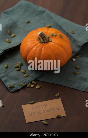 Orangefarbener Kürbis mit Samen auf Holztisch mit halloween-Papierkarte, flacher Fokus Stockfoto