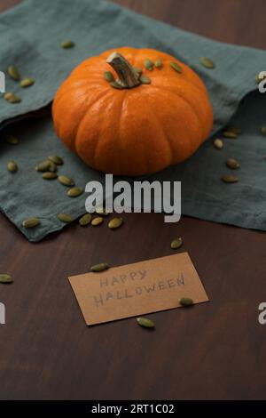 Orangefarbener Kürbis mit Samen auf Holztisch mit halloween-Papierkarte, flacher Fokus Stockfoto