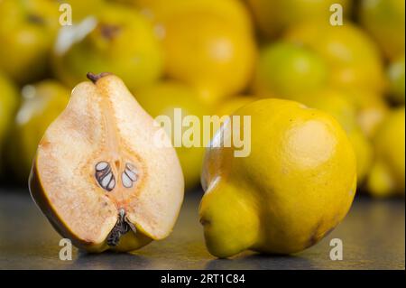 Halbierte und halbierte Quittenfrüchte und ganze Früchte auf einem dunklen Tisch mit einem Haufen anderer Quitten mit unscharfem Hintergrund Stockfoto