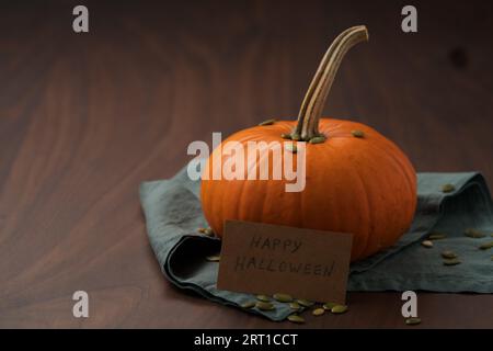 Orangefarbener Kürbis mit Samen auf Holztisch mit halloween-Papierkarte, flacher Fokus Stockfoto