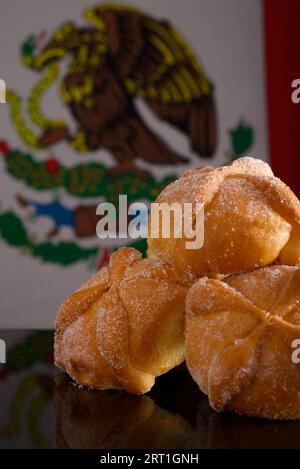 Totes Brot auf schwarzem Glastisch mit mexikanischer Flagge im Hintergrund. Typisches Dessert des Tages der Toten. Stockfoto