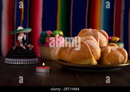 Totes Brot und mexikanisches Kunsthandwerk mit farbenfroher Sarape im Hintergrund. Typisches Dessert des Tages der Toten. Stockfoto