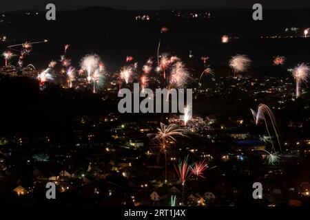 Nachtaufnahme eines Dorfes mit Silvesterfeuerwerk mit mehreren Raketen aus der Vogelperspektive Stockfoto