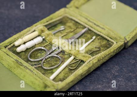 Antike seltene Nähgarderei in offener grüner Samtbox mit Schere, Nähnadeln und Häkelhaken aus Metall und Tierknochen in sehr gutem Zustand Stockfoto