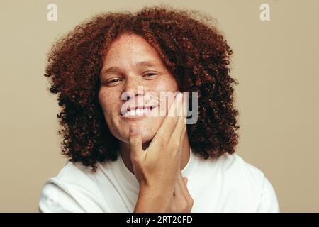 Porträt eines Jugendlichen Mannes mit Ingwerhaaren, die sein schönes, freckeliges Gesicht berühren und stolz auf seine Hautpflege-Routine sind. Glücklicher junger Mann, der sich um ihn kümmert Stockfoto