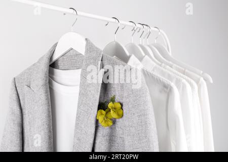 Graue Jacke und weiße Hemden auf dem Gestell, Blume in der Tasche Stockfoto