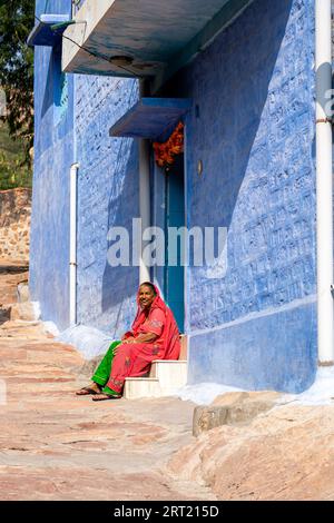 Jodhpur, Indien, 9. Dezember 2019: Eine indische Frau in bunten Kleidern sitzt vor einem blauen Haus Stockfoto