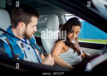 Junge Frau und männlicher Ausbilder sitzen im Auto und legen die Sicherheitsgurte an, bevor sie fahren. Fahrprüfung, Fahrerkurse, Prüfungskonzept Stockfoto