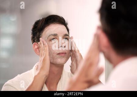 Junger Mann, der abends das Gesicht mit Reinigungsschaum wäscht Stockfoto