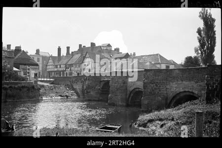 King John's Bridge, Tewkesbury, Gloucestershire, 1940-1948. Ein Blick auf die King John's Bridge, die den Fluss Avon überspannt, in südöstlicher Richtung die Mythe Road hinunter und in Richtung High Street schaut. Der Rand des Westufers des Flusses ist im Vordergrund zu sehen, wobei sich die Brücke von rechts nach links über das Bild erstreckt. Entlang der Mythe Road sind Reihen von Gebäuden zu sehen, darunter ein Fachwerkgebäude mit einem abgeworfenen ersten Stock an der Ecke der Südseite der Straße, das wahrscheinlich das Black Bear Inn ist. Auf der Nordseite der Straße befindet sich das Ende eines Gebäudes mit großen Plakaten an der Seite, eines davon Stockfoto