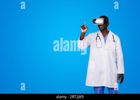 Frohe Millennial african american man Doctor in weißem Mantel und vr-Brille steuert mit dem Finger auf abstrakte virtuelle Tafel Stockfoto