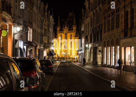 BRÜGGE, BELGIEN - 19. FEBRUAR 2016: Blick auf die Steenstraat bei Nacht in Richtung St. Salvator's Cathedral. Geschäfte, Autos und die Unschärfe von Menschen können s sein Stockfoto