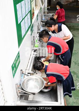 (230910) -- HAIKOU, 10. September 2023 (Xinhua) -- Fu Yaohui (zurück) unterrichtet die Schüler, wie sie ihr Geschirr nach einem Essen in der Hainan (Haikou) Special School in Haikou, Südchinesische Provinz Hainan, am 6. September 2023 reinigen. Fu Yaohui ist Lehrer an der Sonderschule in Haikou. Seit 2004 engagiert sich Fu in Sonderpädagogik für Schüler mit geistiger Behinderung, um ihre Grundfertigkeiten zur Anpassung an das Leben zu entwickeln. Jeden Tag kommt Fu früh in die Schule und begleitet die Schüler mit Geduld und Ermutigung. „Ich möchte, dass meine Schüler selbstständig sind“, sagte sie. Um das zu erreichen Stockfoto