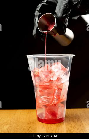 Das Mädchen gießt Erdbeersirup in ein Plastikglas mit Eiswürfeln. Der Prozess der Herstellung von Blasentee. Stockfoto